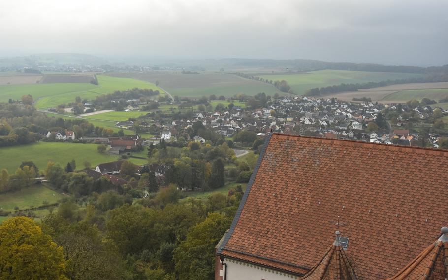 A sprawling view of hazy clouds, green hills and a distant village stretches beyond a red-tiled roof.