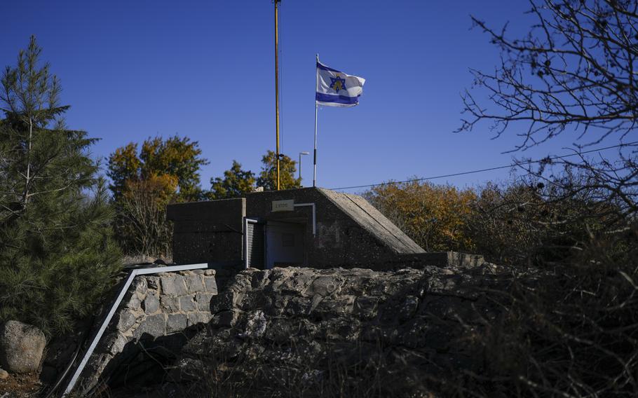 A cement bomb shelter is seen surrounded by trees and with an Israeli flag on top of it.