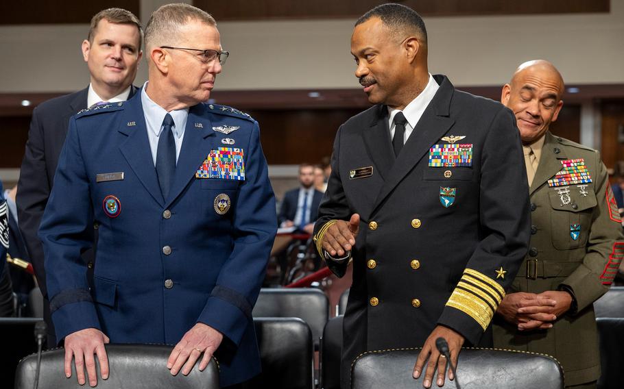 Two men in military uniforms standing behind chairs as they talk.