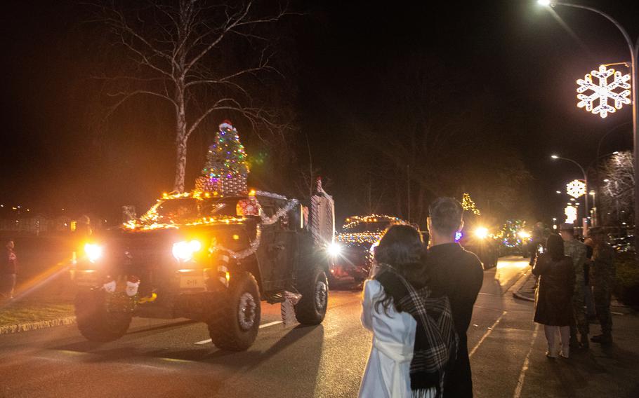 A parade is highlighted by an Army vehicle covered in lights and carrying a Christmas tree.