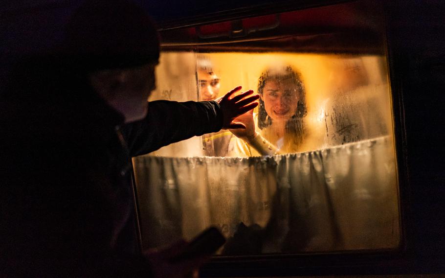 A woman looks through a train window and holds up her hand to meet her husband’s