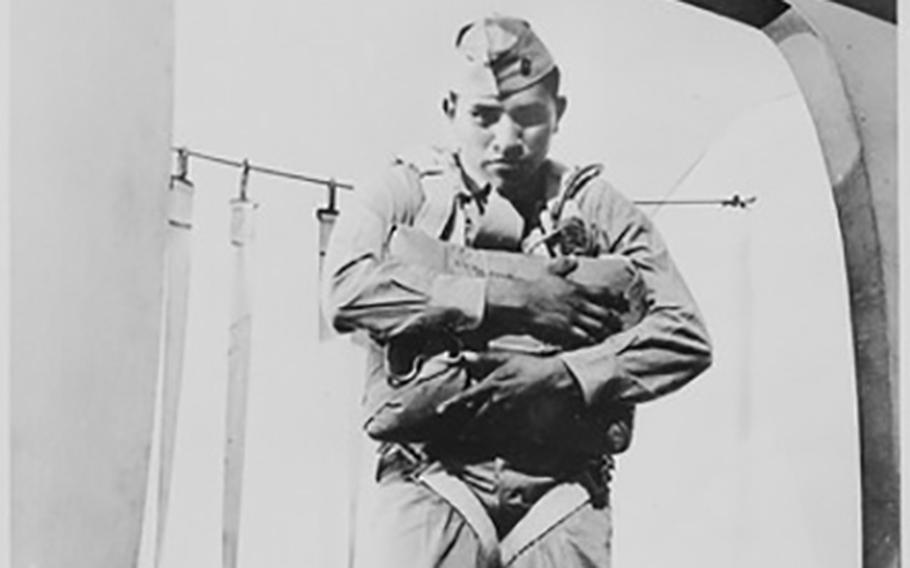 A black-and-white, 1940s-era image of a Marine in uniform clutching a parachute while standing in the doorway of an airplane.