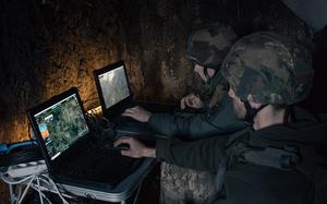 Ulysses and another soldier monitor footage from a reconnaissance drone from devices set up in a foxhole.