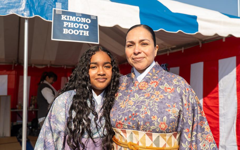 A teenage girl stands next to a woman, both are wearing light blue kimonos. 