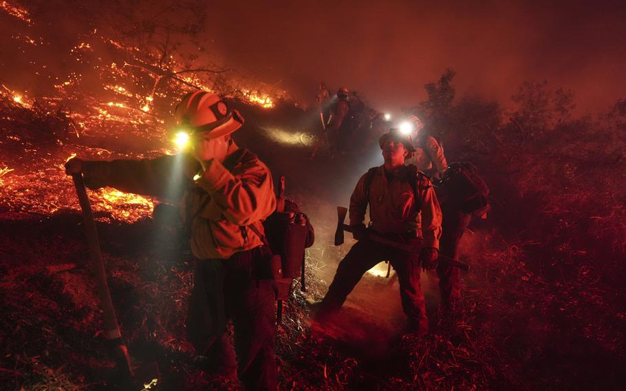 Flames light up the landscape behind firefighters.