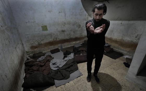 A man stands in a prison cell with his hands together to demonstrate how he was bound and tortured.