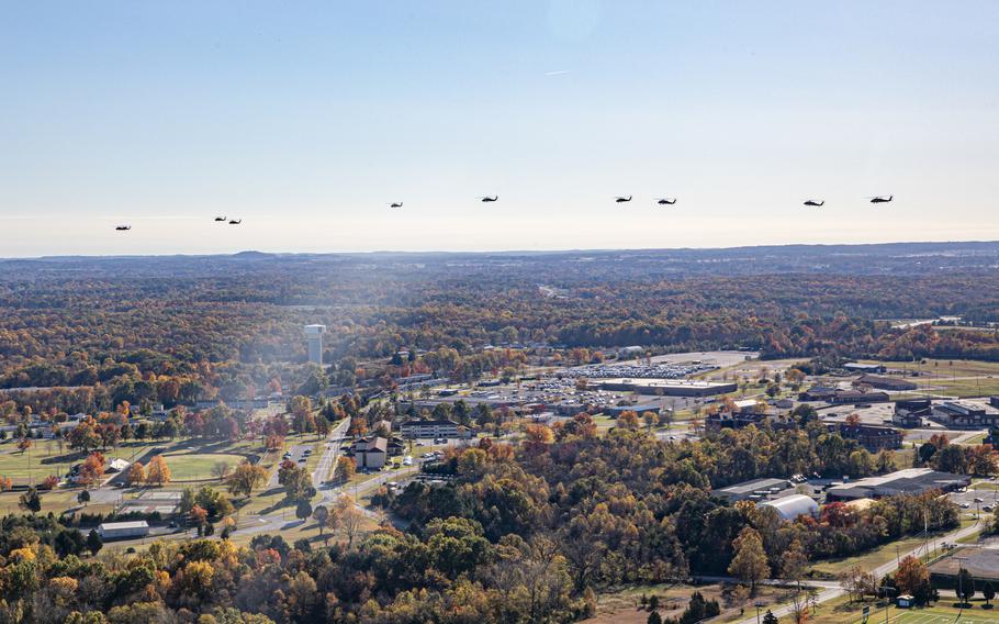 Helicopters in a row over a mass of trees and low-rise buildings.