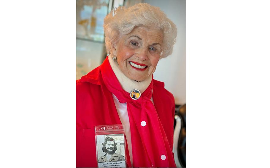 An elderly woman poses while wearing a red shirt and scarf.