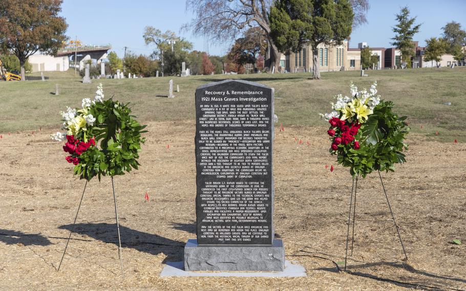 A granite monument is flanked by wreaths in a cemetary.