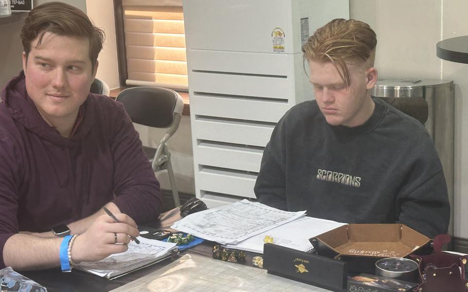 Two men sit at a table with Dungeons and Dragons character sheets and dice.