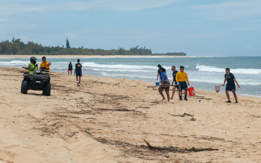 Navy volunteers pick up trash and debris on a beach.