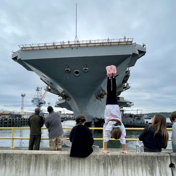 Rori Fox, 10, performs a handstand to welcome her father, Lt. Cmdr. Joshua Fox, an officer on the USS Ronald Reagan. The carrier arrived at Naval Base Kitsap on Aug. 13, 2024. It will go into a six-month maintenance at the Puget Sound Naval Shipyard.