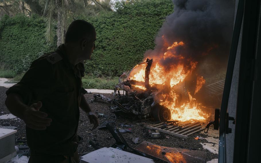 Soldiers and civilians try to extinguish a car on fire after a missile attack in the city of Ashkelon, Israel, on Tuesday, Oct. 10, 2023.