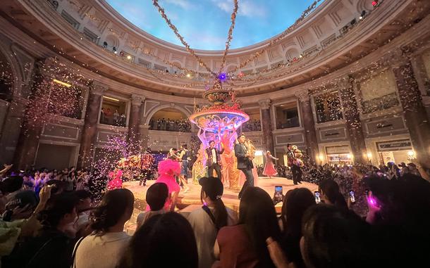 Viewers gather around a circular stage as performers dance and play instruments.