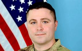 Staff Sgt. Jonathan Lane stands in front of a flag in an Army uniform.