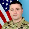 Staff Sgt. Jonathan Lane stands in front of a flag in an Army uniform.