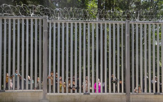 FILE - Members of a group of some 30 migrants seeking asylum in Bialowieza, Poland, on Sunday, 28 May 2023, look through the railings of a wall that Poland has built on its border with Belarus to stop massive migrant pressure. (AP Photo/Agnieszka Sadowska, File)