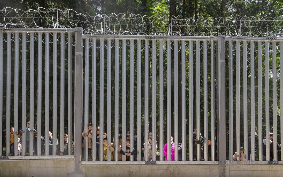 Members of a group of some 30 migrants seeking asylum in Bialowieza, Poland, on Sunday, 28 May 2023, look through the railings of a wall that Poland has built on its border with Belarus to stop massive migrant pressure. 