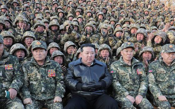 Kim Jong Un, clad all in black, poses with a crowd of North Korean military members in uniform. 