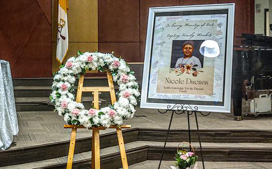 A portrait of DODEA speech teacher Nicole Duenas and a wreath stand at the front of a church during a memorial service.