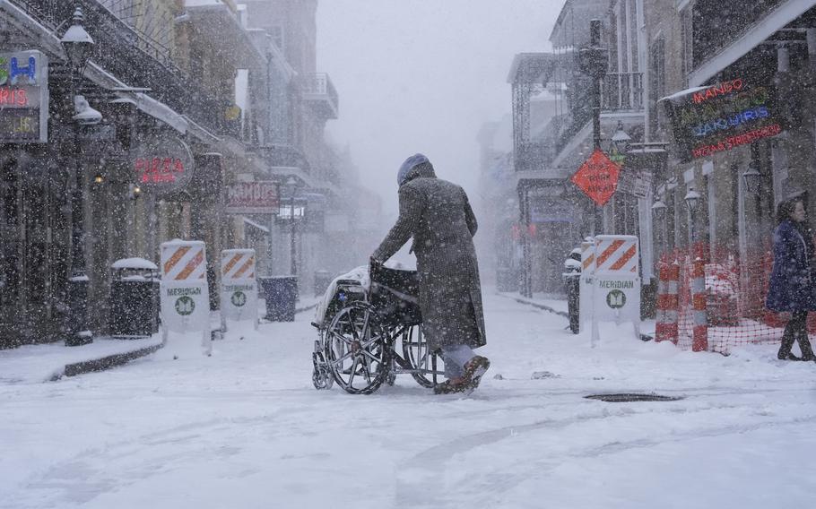 A person in a coat pushing a wheelchair is seen in the center of the photo on a snowy street.