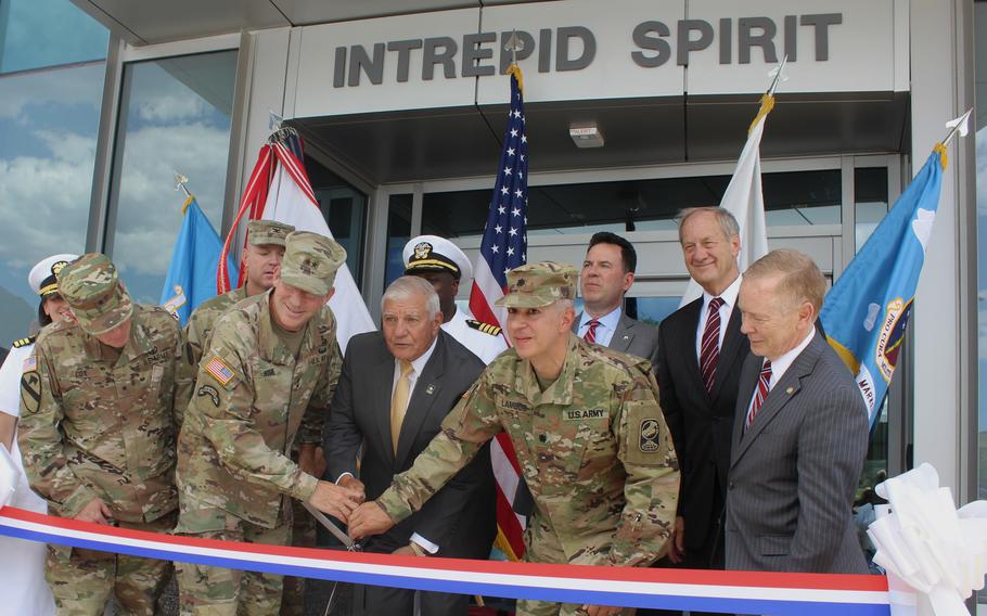 Soldiers and men in suits cut a ribbon in front of a doorway.