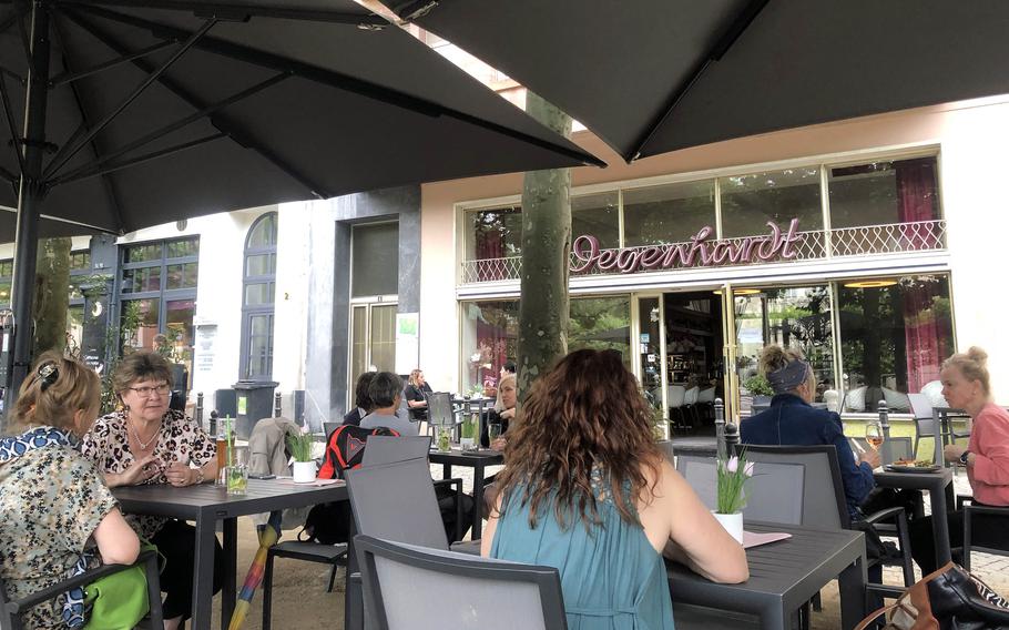 Diners at Degenhardt in Wiesbaden, Germany, sit outside under umbrellas. Note the 1950s facade with the restaurant name written in cursive.