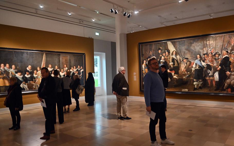 Visitors check out some of the monumental paintings in the exhibit “Rembrandt’s Amsterdam. Golden Times?”  The paintings by Nicholas Eliasz Pickenoy, left, and Govaert Flinck, depict companies of crossbowmen. The exhibit at the Städel in Frankfurt runs until March 23, 2025.