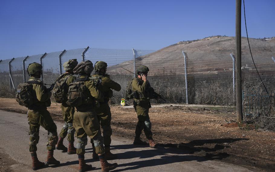 Five Israeli soldiers on patrol by a perimeter fence.