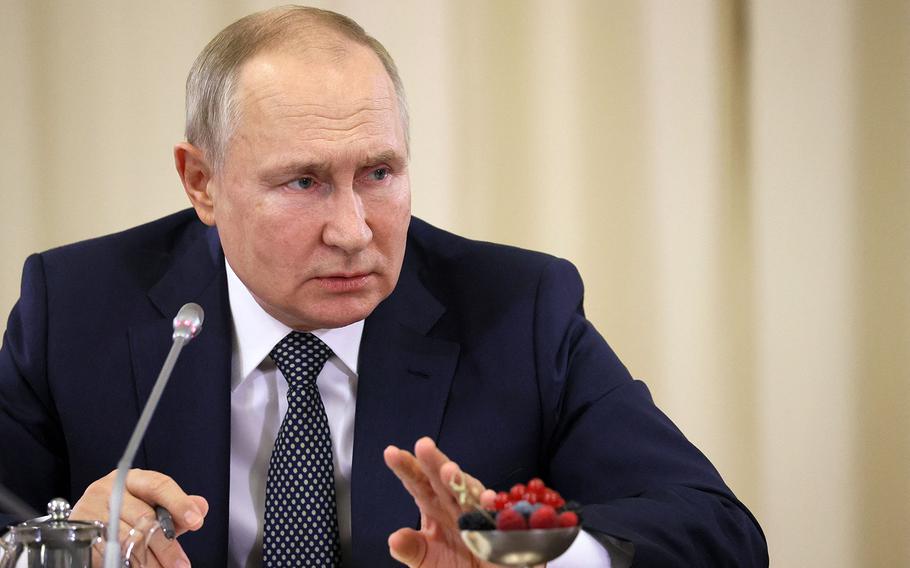 Russian President Vladimir Putin sits at a table with various fruits in front of him as he speaks into a microphone.