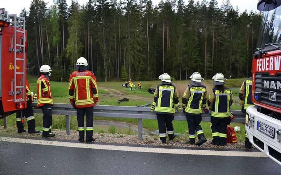 Local firefighters look at the wreckage of a car in a field near Bayreuth, Germany, May 15, 2021. A 23-year-old U.S. service member was seriously injured in the accident on the A9 autobahn.