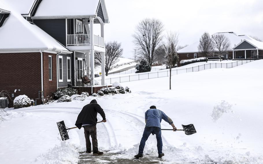 Two men shovel snow off the driveway of a home.