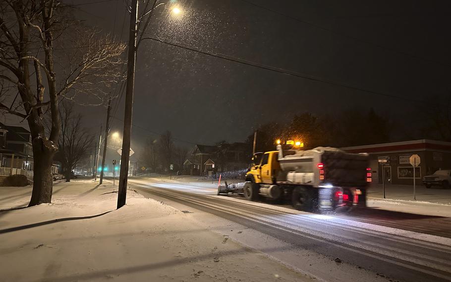 A snowplow moves along a street at night.