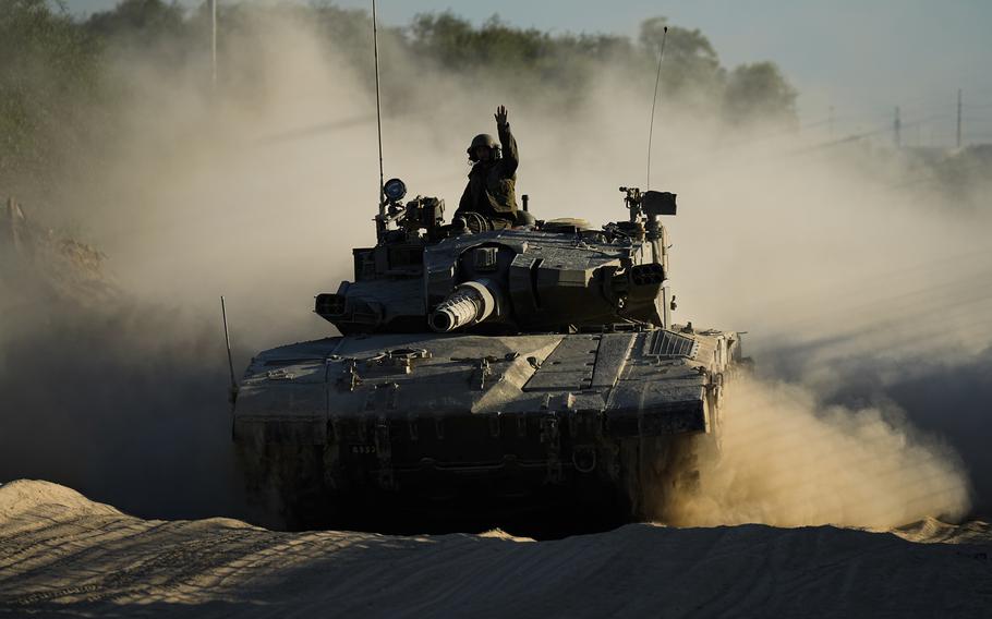 A soldier sits in the tower of a tank as it advances along a dirt road.