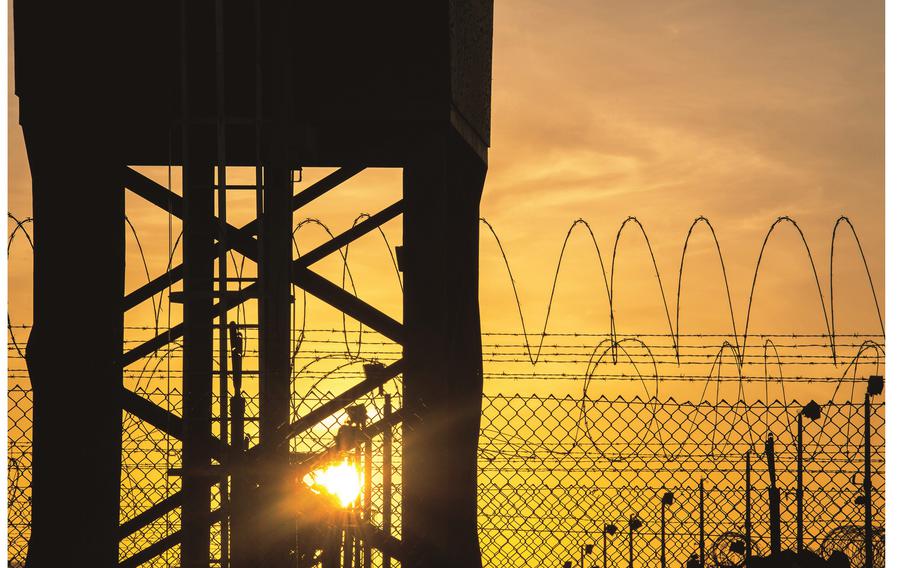 The rising sun silhouettes an out-of-use guard tower, fence and concertina wire 