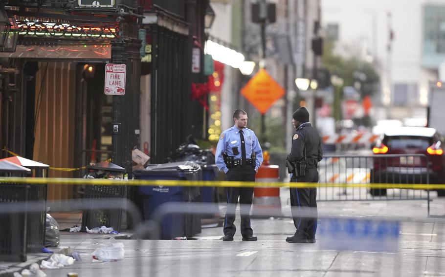 Two people in emergency services uniforms stand behind police tape.