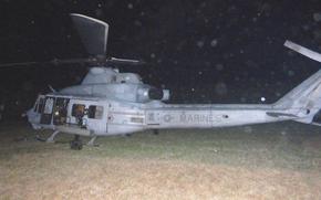 A Marine helicopter sits in a grassy field in darkness.