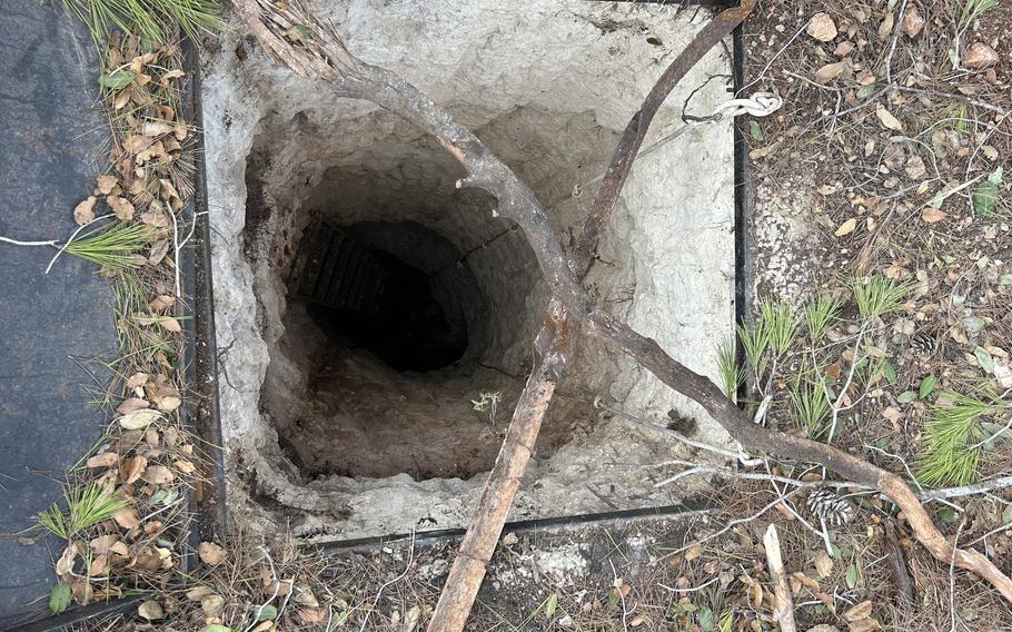 A deep hole in the ground is shown partially obscured by sticks.