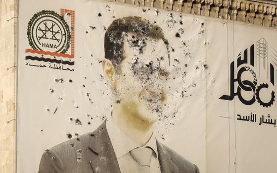 A large image of Syrian President Bashar Assad on the side of a government building is riddled with bullet holes.