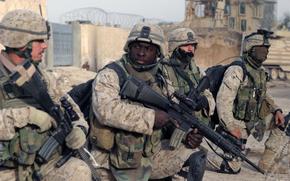 Four Marines in uniform, three of them holding weapons, kneel as they prepare to patrol Fallujah, Iraq. 