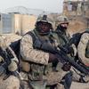 Four Marines in uniform, three of them holding weapons, kneel as they prepare to patrol Fallujah, Iraq. 