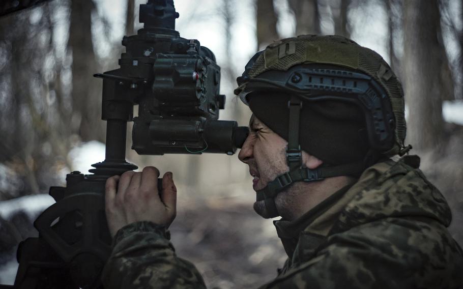 A serviceman squints as he looks through a sight for targeting artillery.