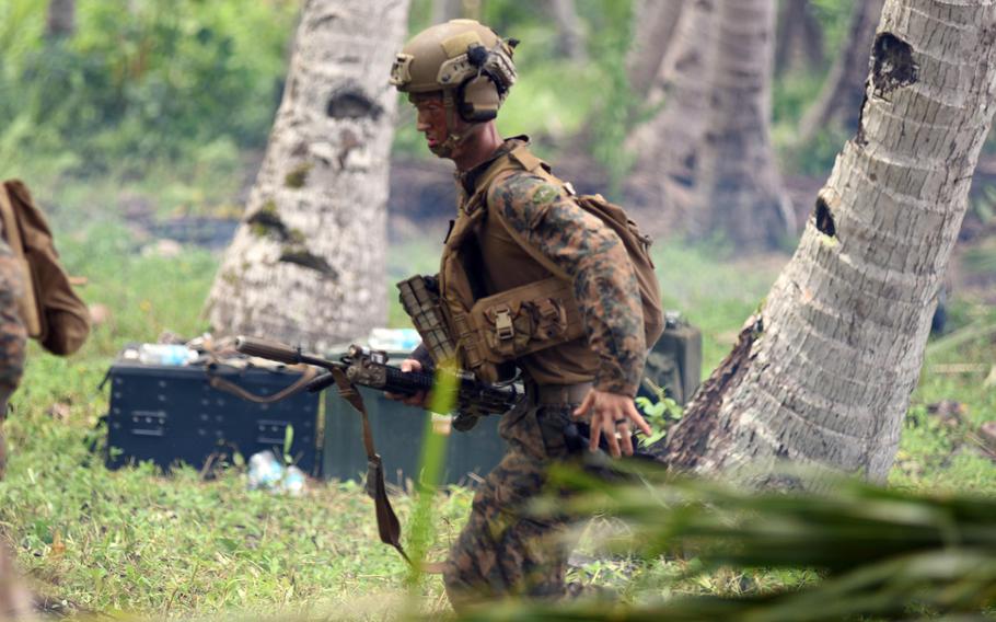 A Marine in combat gear and carrying a machine gun walks between palm trees during an exercise.