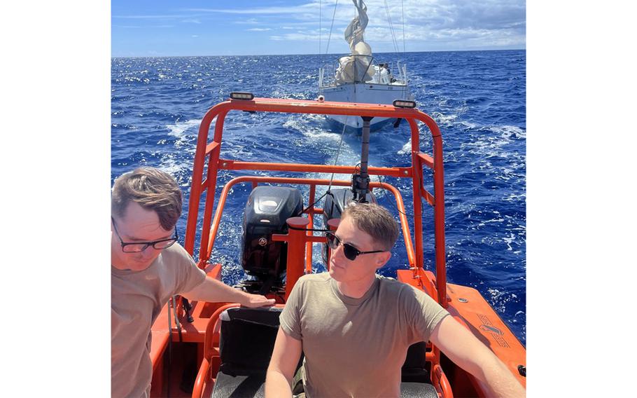 Two soldiers drive a boat pulling a sailboat on the ocean.