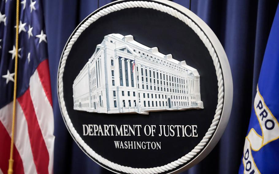 The seal of the Department of Justice is displayed next to a U.S. flag.