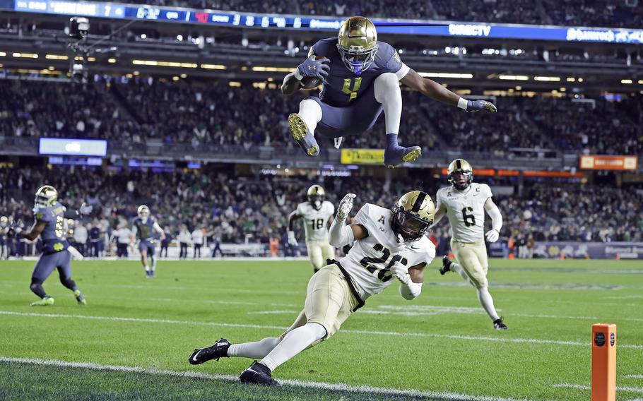 A Notre Dame football player jumps over an Army football player who is running.