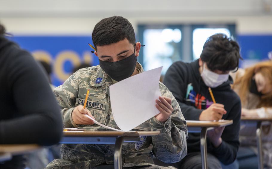 Students wearing facemasks sit at desks while taking a test using paper and pencils.