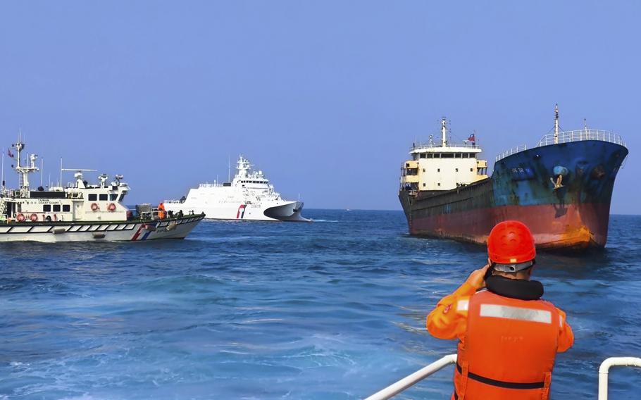 A man in an orange uniform watches as two white ships rest near a larger black cargo ship.