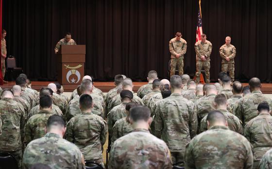 Speakers on the stage and troops in the audience bow their heads.