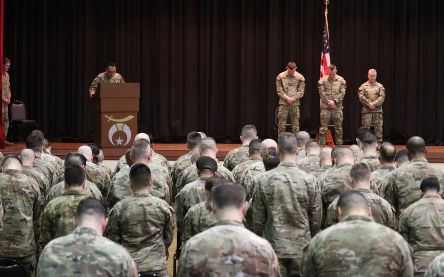 Speakers on the stage and troops in the audience bow their heads.